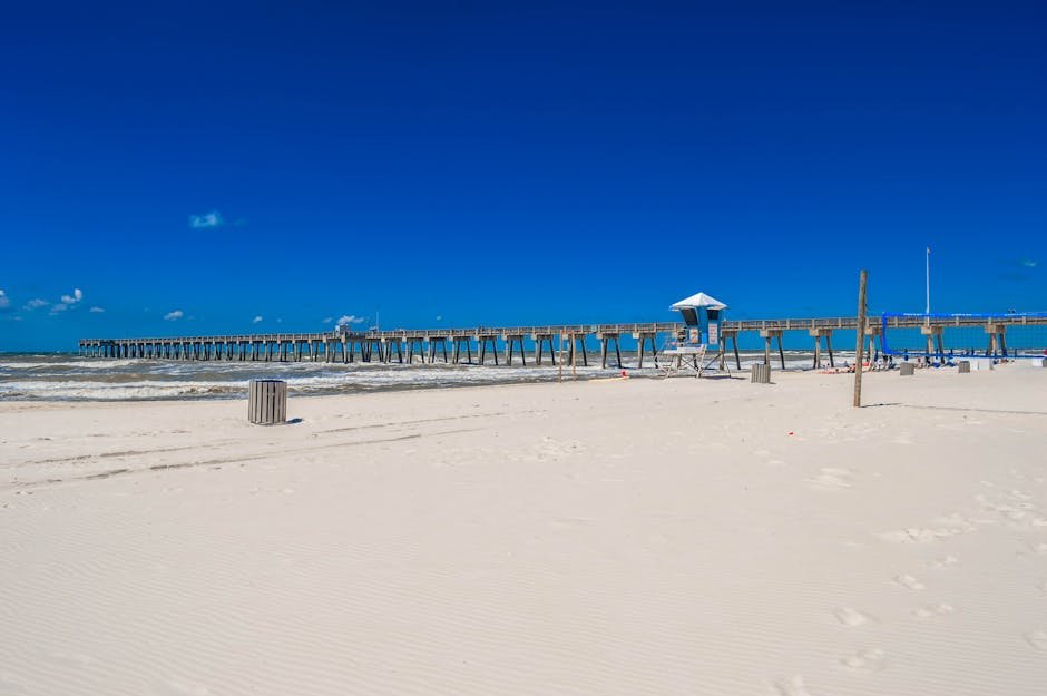 Pristine white sandy beach with a scenic pier under a clear blue sky in Panama City Beach, Florida.